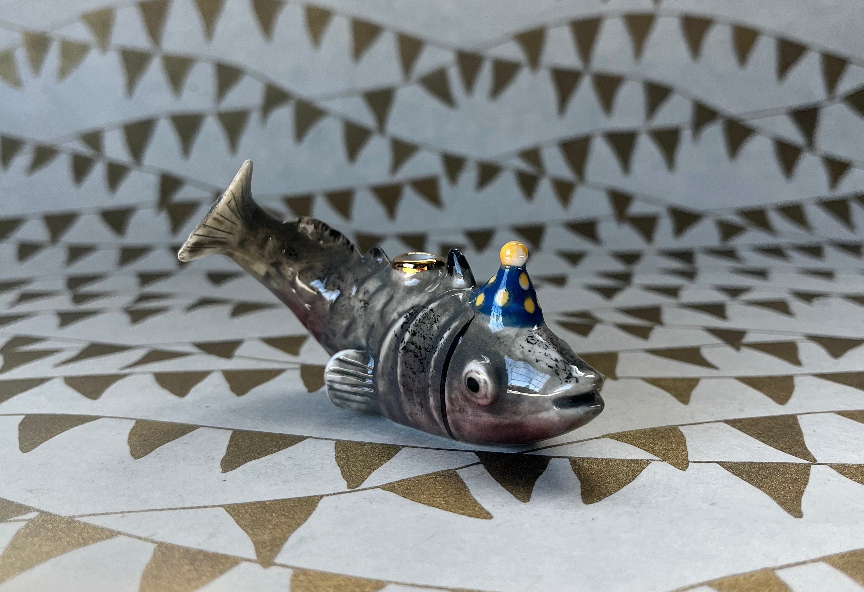 Metallic silver fish cake topper with small figurine rider on geometric patterned surface