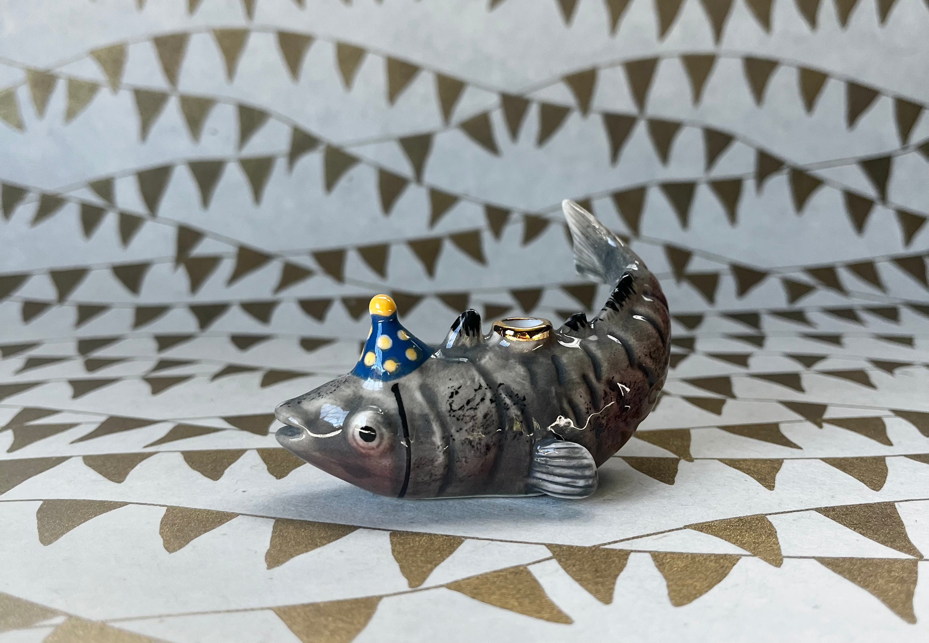 Gray ceramic fish cake topper lying on back wearing blue party hat