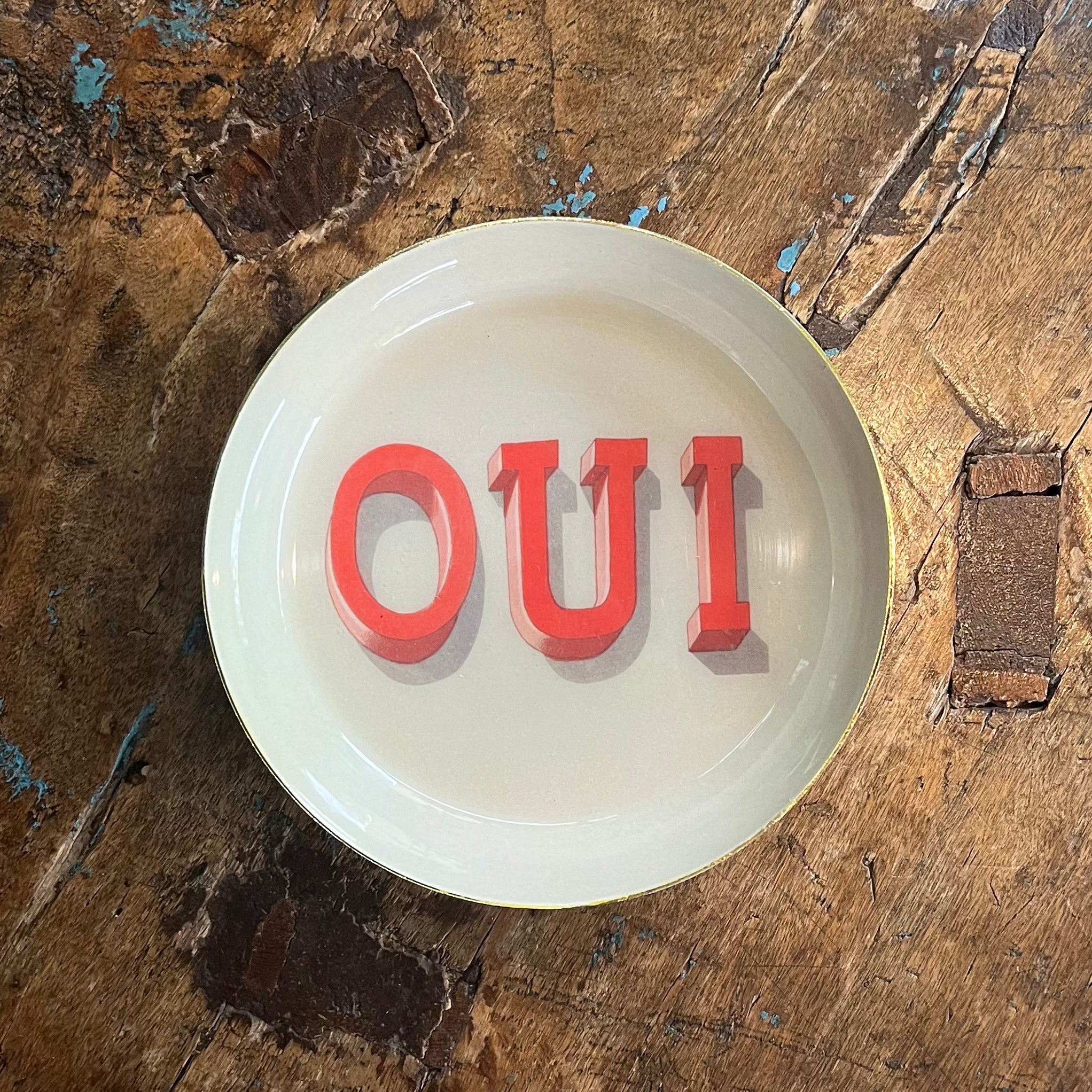 Round white OUI tray with red lettering on worn wooden surface