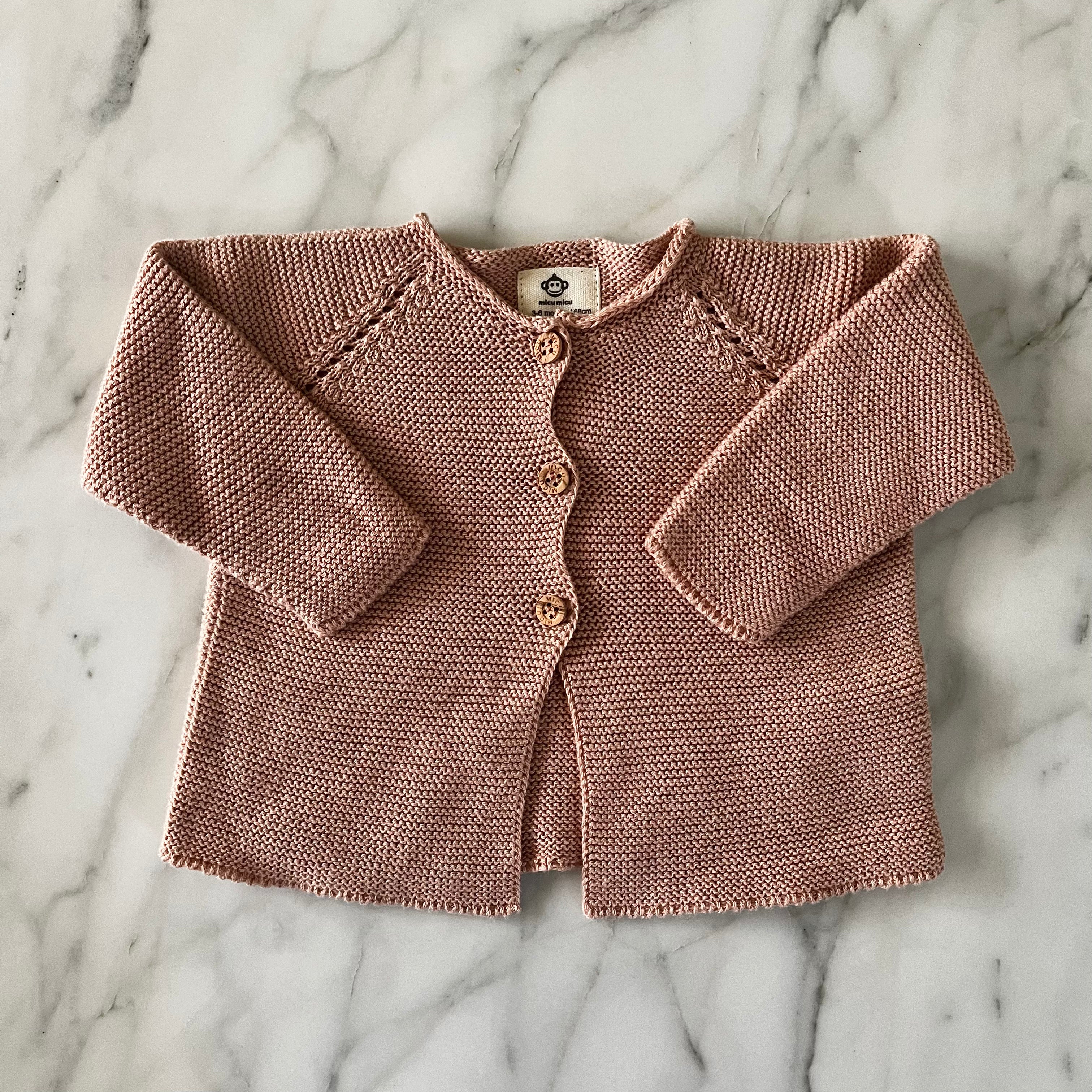 Dusty rose knit baby cardigan with buttons laid flat on marble surface