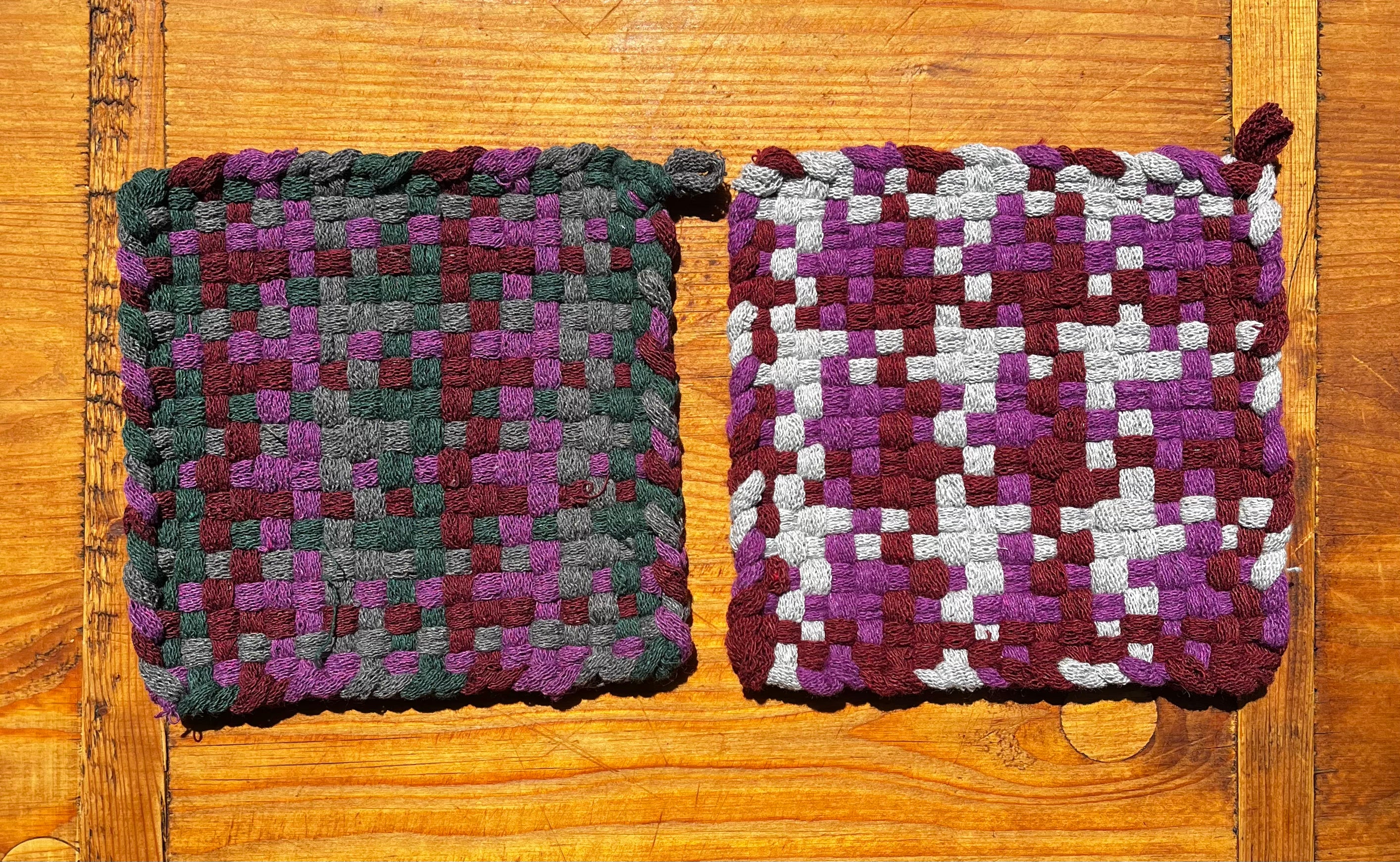 Two woven Squished Grapes Potholders in purple, burgundy, gray, and white checkered pattern on wooden surface