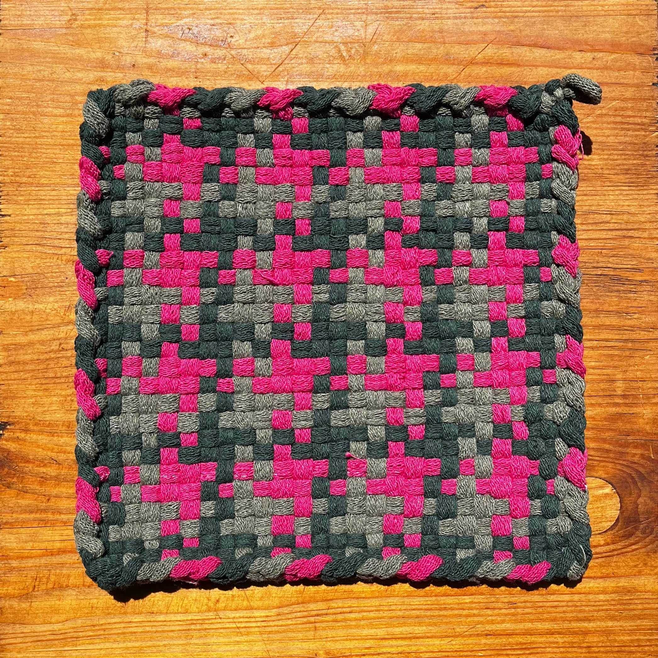 Woven watermelon potholder with pink and gray checkered pattern on wood surface