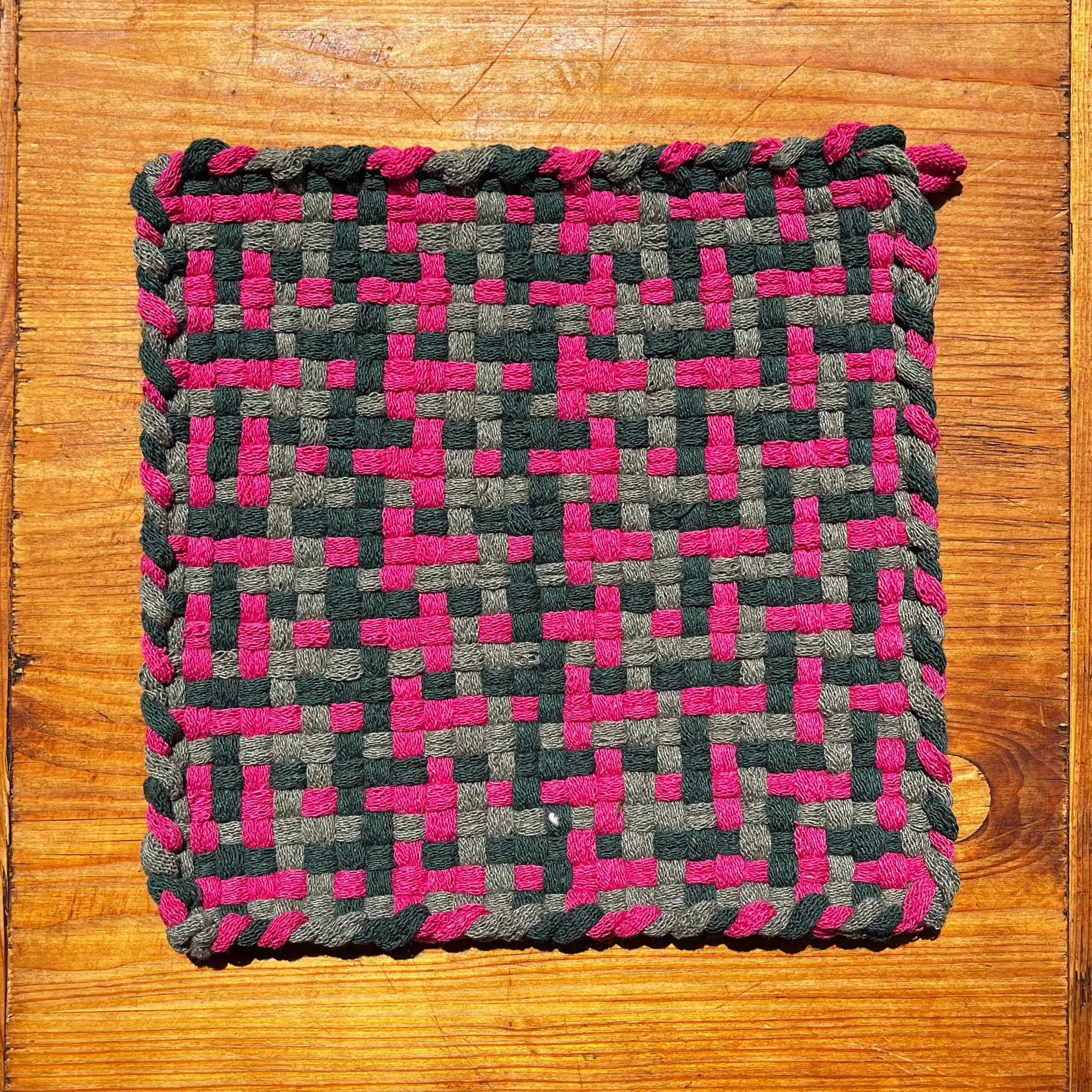 Flower Fields Potholder with woven pink and dark gray checkered pattern on wood surface