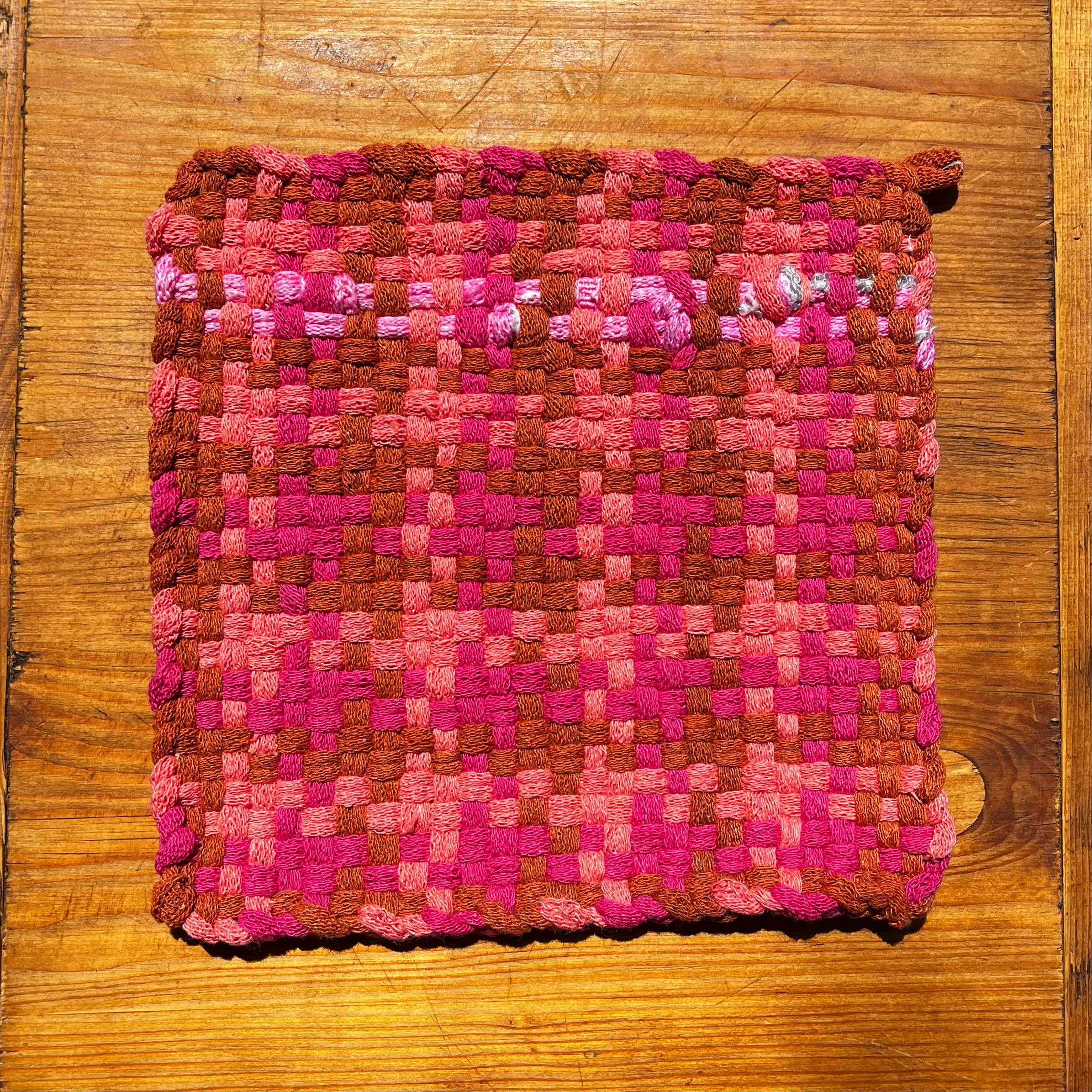 Pinky and Perky Potholder in woven pink and brown checkered pattern on wooden surface