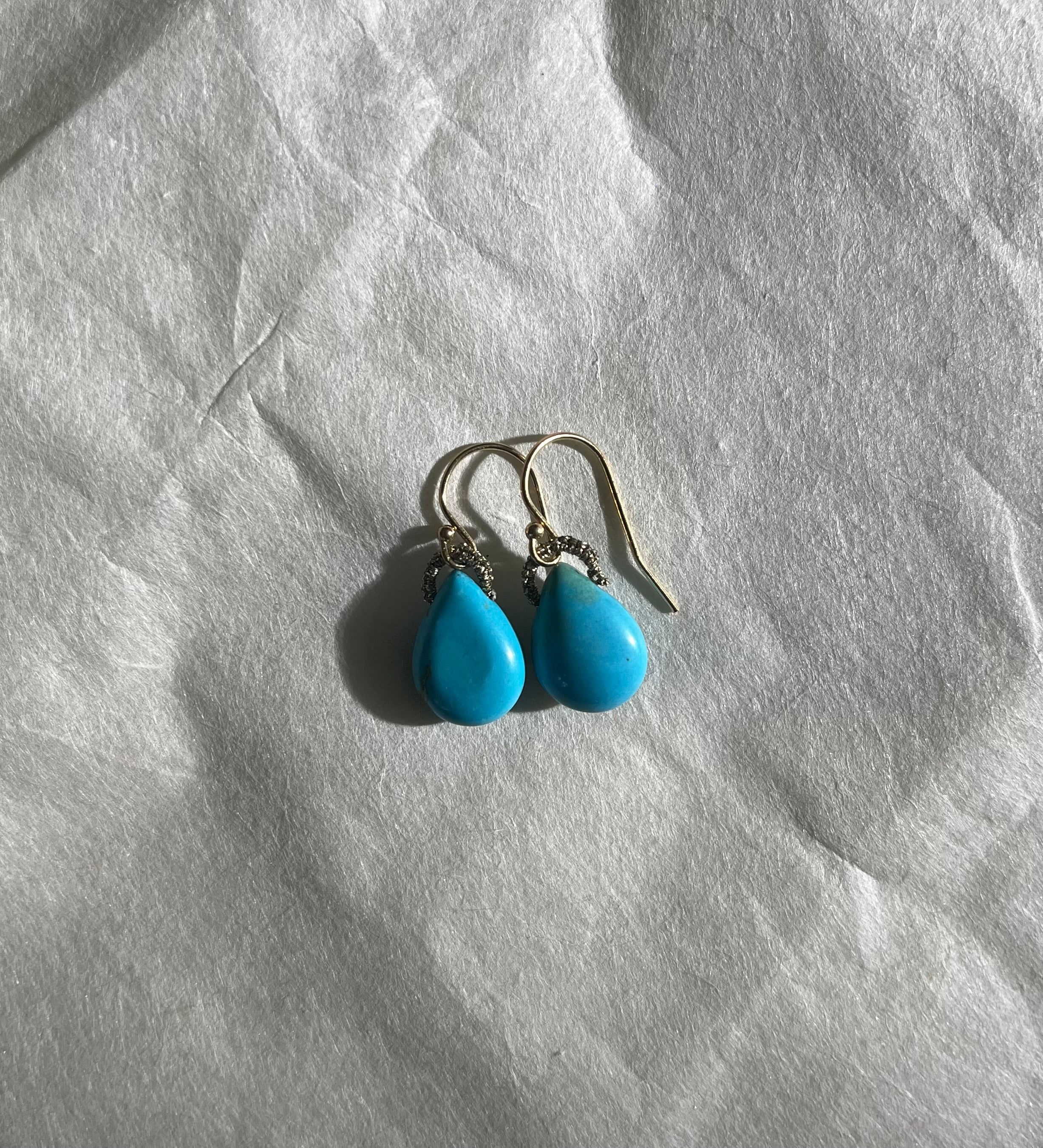 Pair of turquoise drop earrings with gold hooks on white textured background