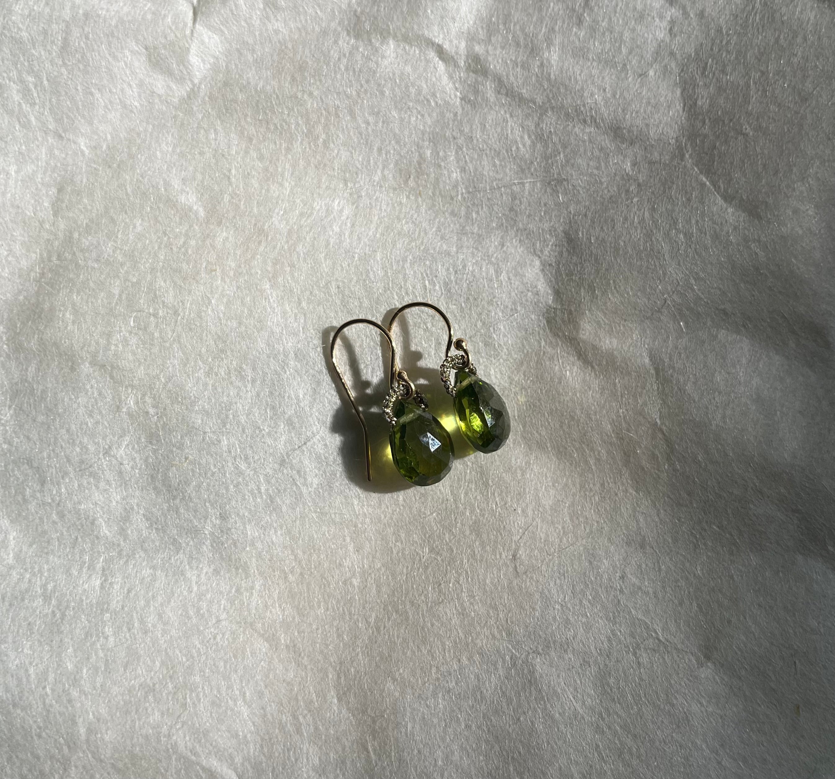 Peridot drop earrings with faceted green stones on gold wire hooks on white textured surface