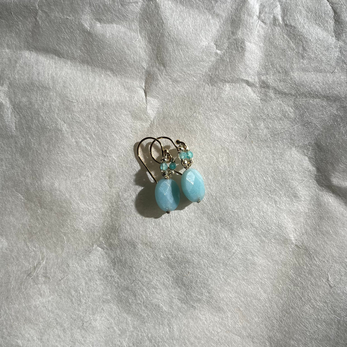 Pair of amazonite earrings with turquoise drops and beaded halos on white textured surface
