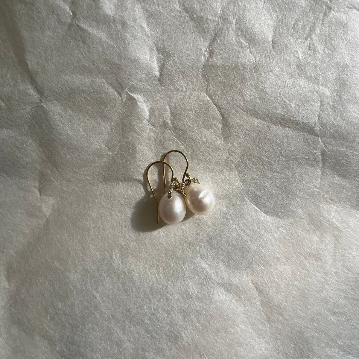 White pearl earrings with gold hooks lying on textured white fabric