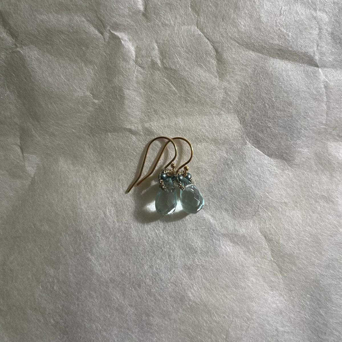 Pair of aquamarine drop earrings with pearl accents on gold hooks, placed on white fabric