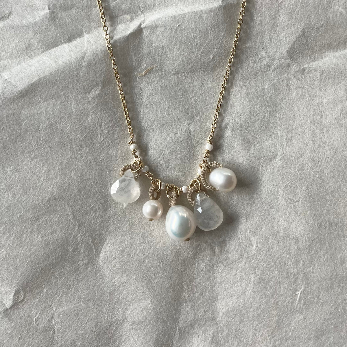 Gold chain necklace with clustered white pearls and translucent moonstone teardrop charms on fabric