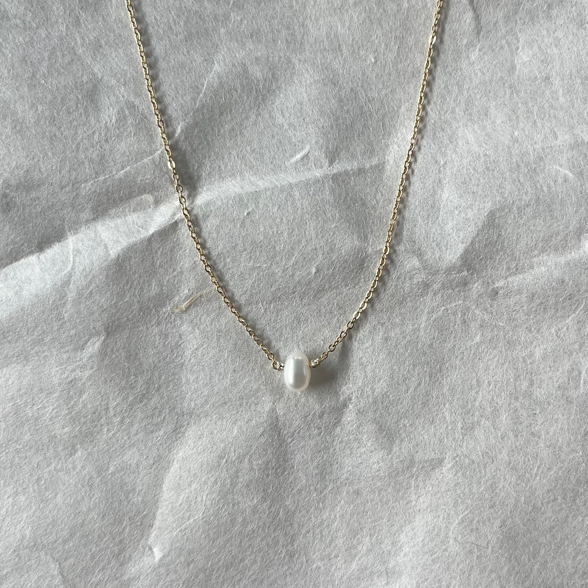 Delicate gold chain necklace with single white freshwater pearl pendant on gray fabric