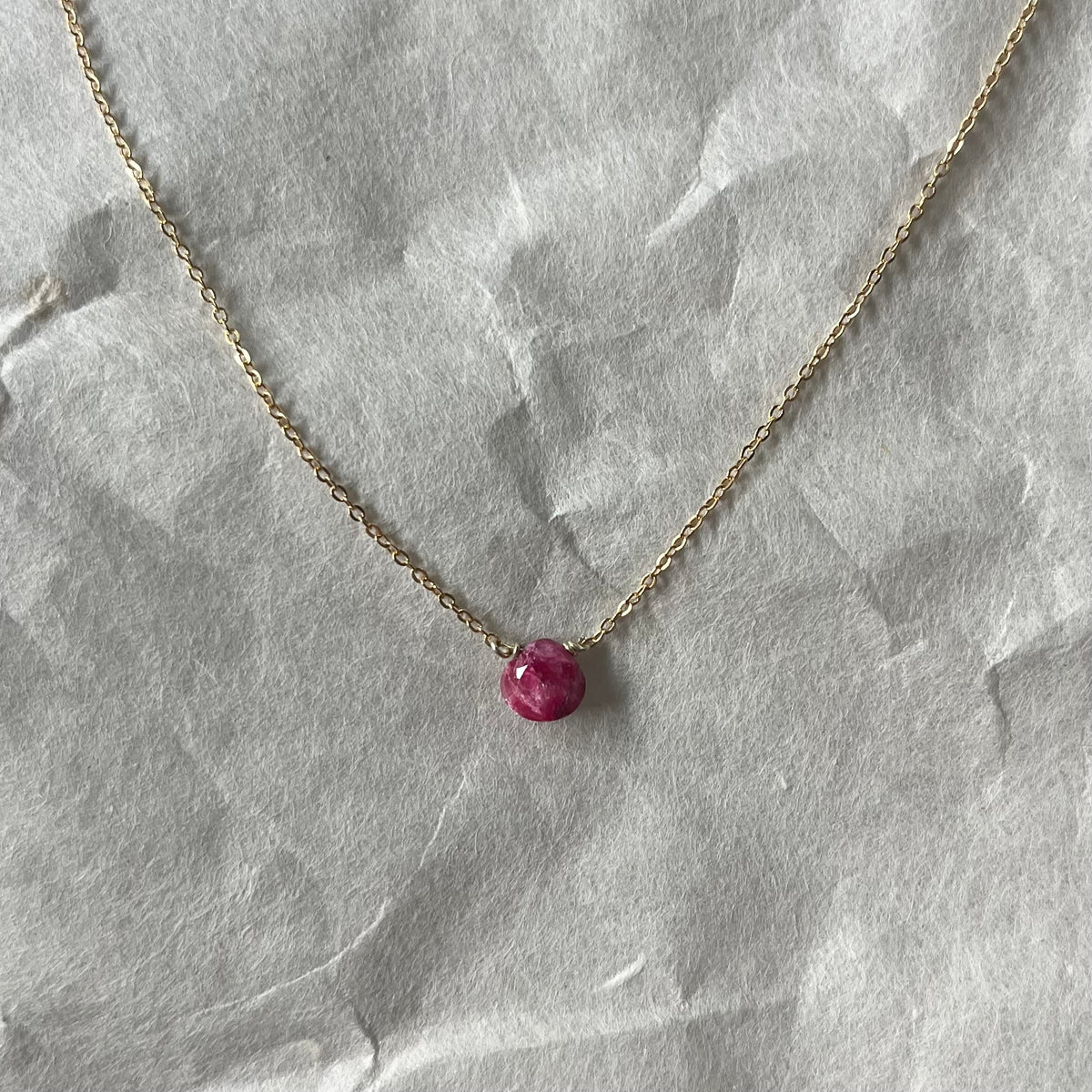 Gold chain necklace with round pink cabochon ruby pendant on white fabric