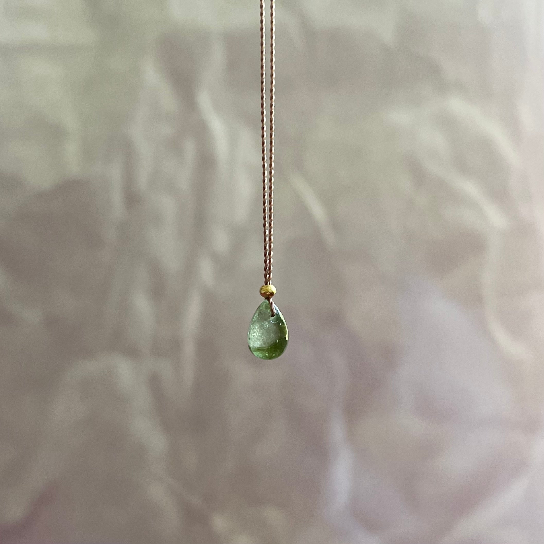 Green tourmaline teardrop pendant on delicate gold chain against soft floral background