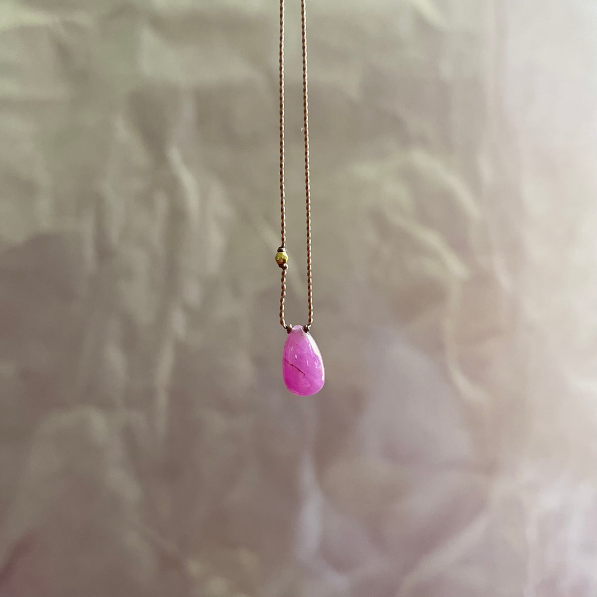 Cabochon ruby teardrop pendant on delicate gold chain against white floral background