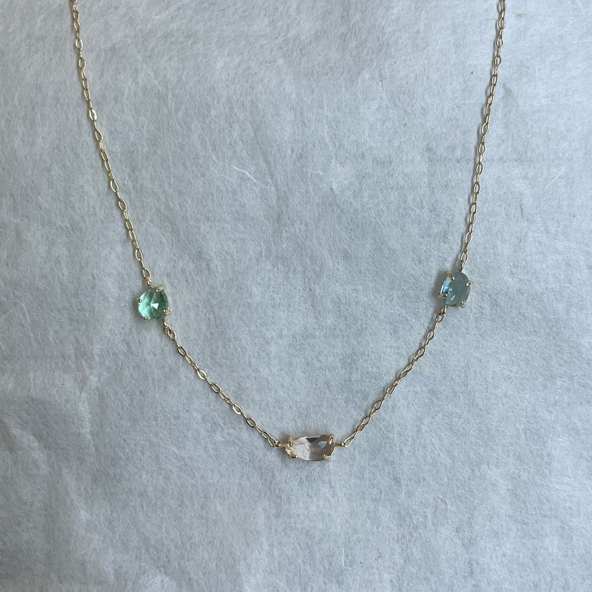 Delicate gold chain necklace with three oval gemstones in blue and clear tones