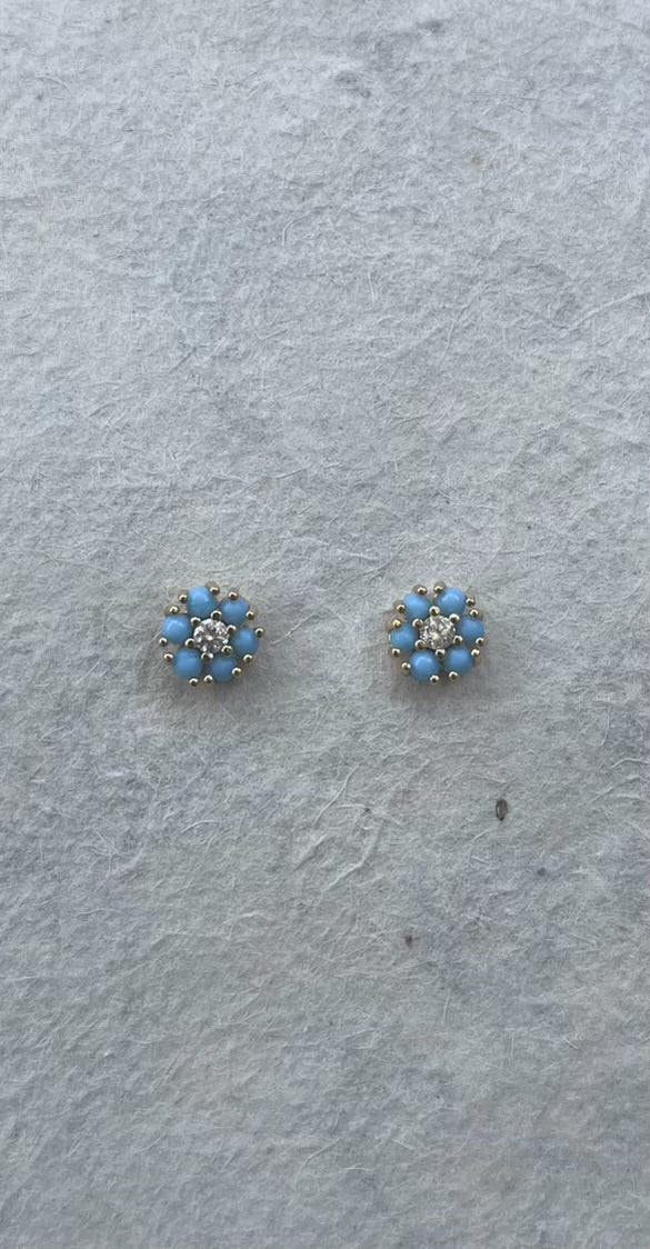 Pair of turquoise and CZ stud earrings in flower cluster design on gray surface
