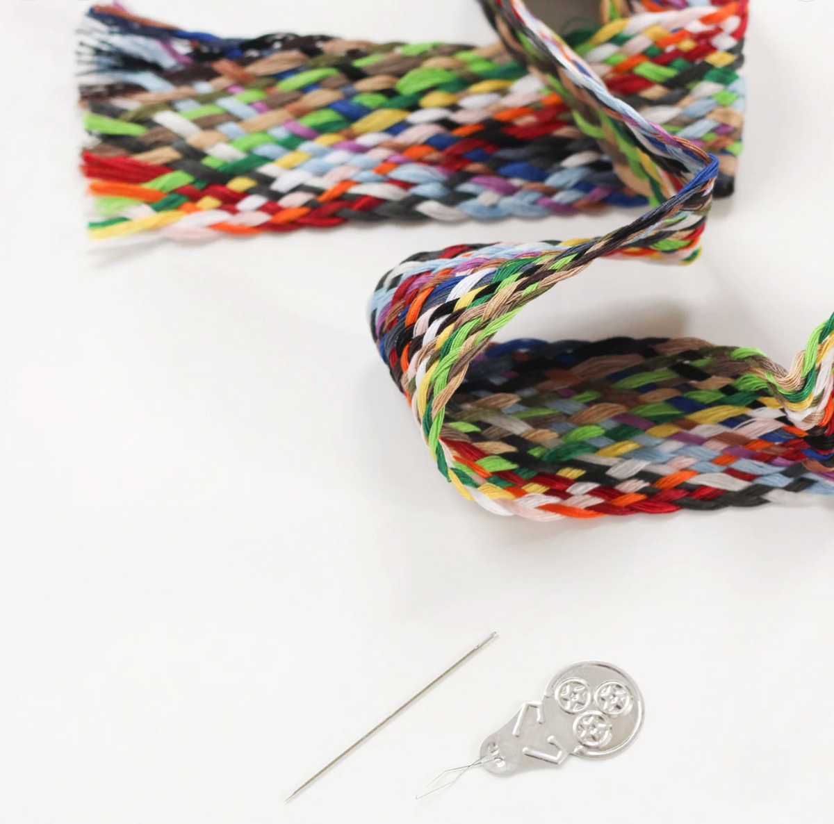 Colorful braided cotton thread bundles with loose strands and silver needle on white background
