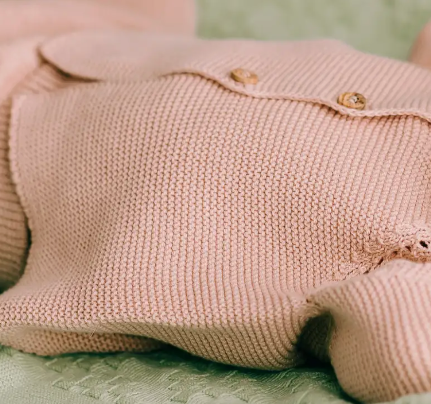 Pink knit baby jacket with buttons and matching pants laid flat