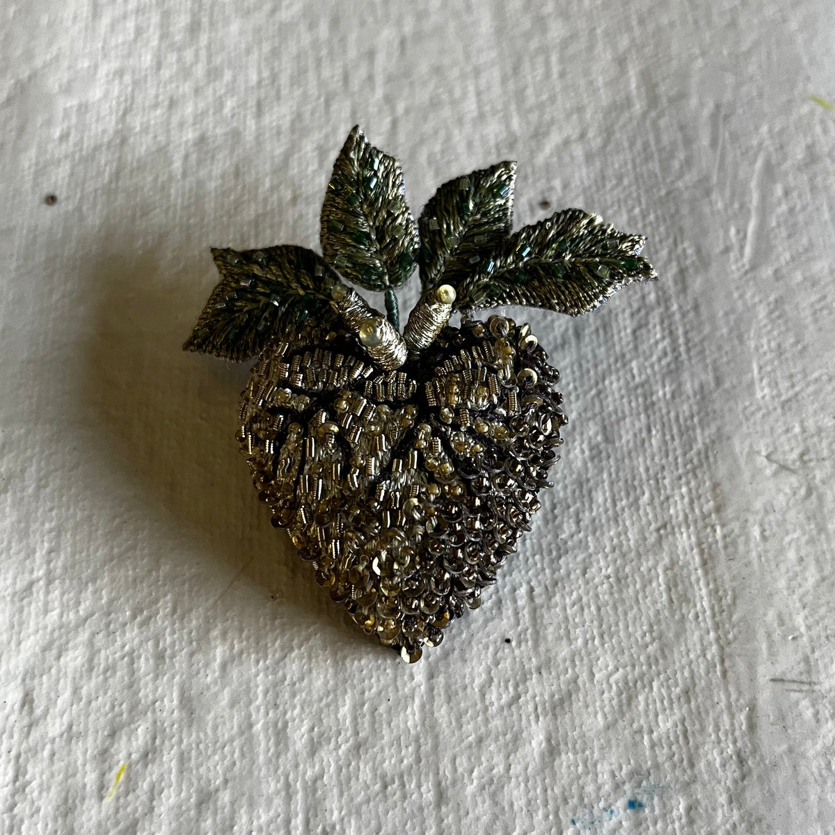 Textured silver-tone Vine Heart Brooch with metallic leaves on white textured fabric